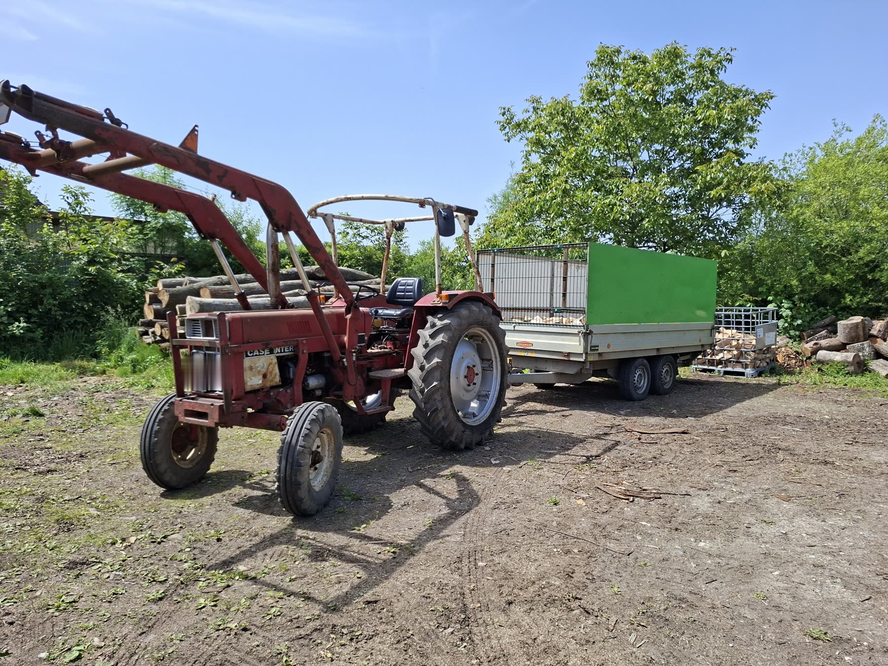 Traktor mit Anhänger und gefüllter Holzbox auf dem Lagerplatz